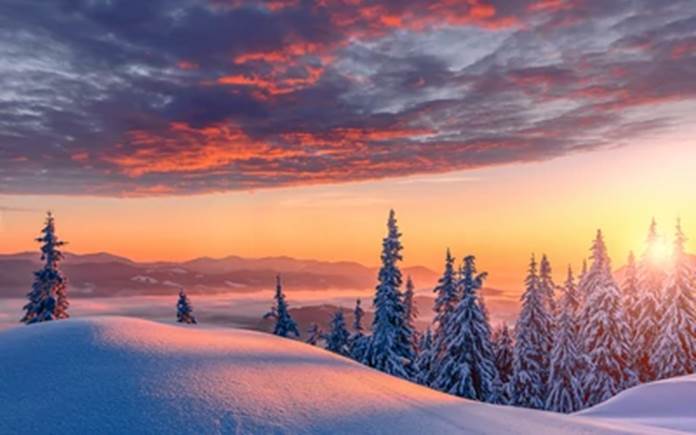 na pierwszym planie znajduje się pokryte śniegiem wzgórze oraz wierzchołki pokrytych śniegiem drzew iglastych, w tle ośnieżone szczyty gór, zachód słońca i chmury na niebie