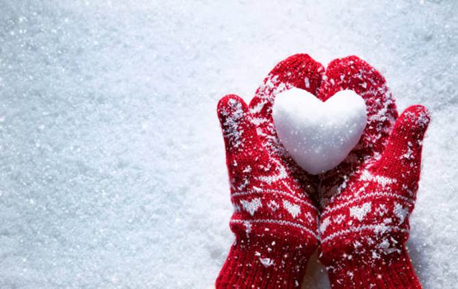 Ułożone na tle śniegu złożone dłonie, ubrane w czerwone rękawice, trzymające kulkę śniegu w kształcie serca 
